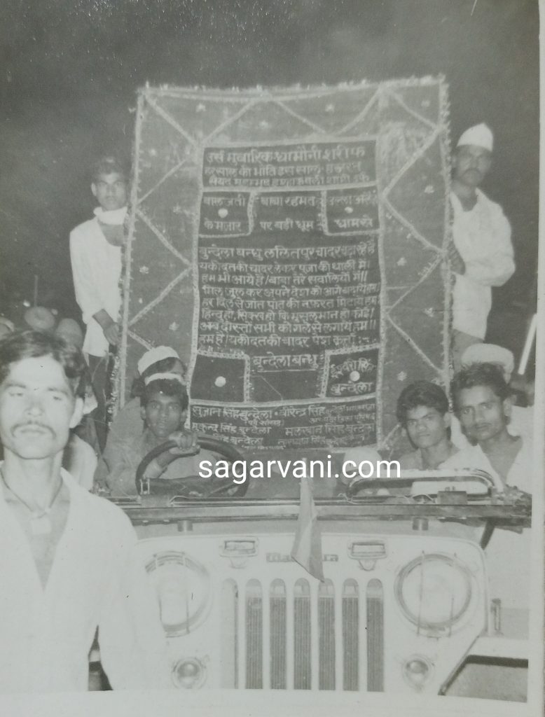 यह चित्र मोहर्रम के जुलूस का नहीं है। आलेख के साथ इसलिए अटैच है क्योंकि ये भी एक चर्चित फोटो है। जिसमें ललितपुर के मशहूर बुंदेला बंधु की तरफ से सागर के धामोनी शरीफ में जीप से चादर पेश की जा रही है। नीचे पूर्व सांसद सुजानसिंह बुंदेला का नाम है। जिनके बेटे गुड्डू राजा बुंदेला हाल ही में सागर से लोकसभा का चुनाव लड़े थे।